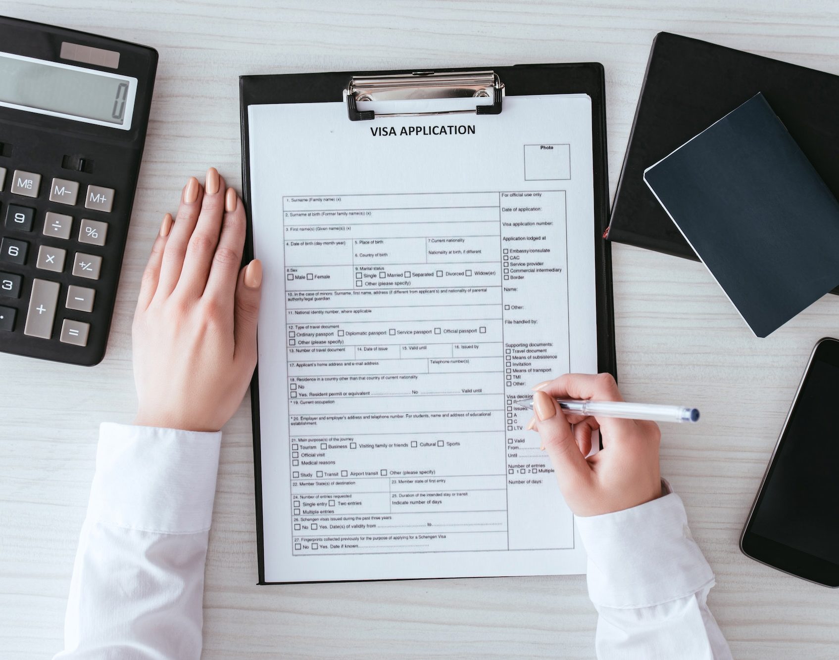 top-view-of-woman-holding-pen-near-document-with-visa-application-lettering-near-smartphone-with-e1692632864660.jpg